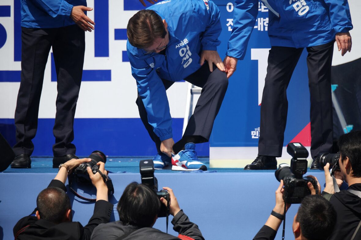 Candidato Lee Jae Myung trocando de sapato em campanha.